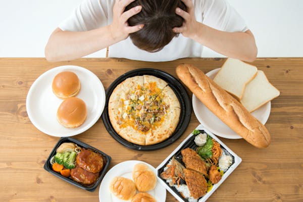 揚げ物やパンなどのカロリーの高そうな食事の前で頭を抱える男性
