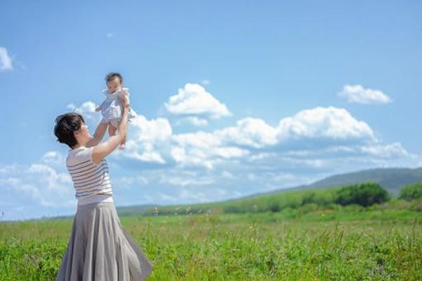 青空の下で赤ちゃんをたかいたかいする女性