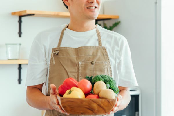 野菜のはいったかごを持ったエプロンの男性