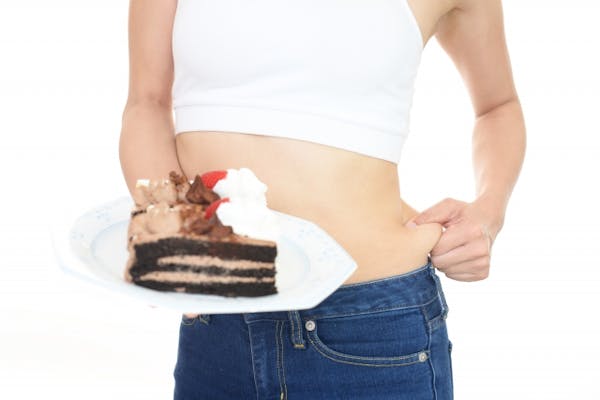 ケーキののったお皿を持って自分の脇肉をつまんでいる女性
