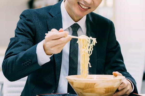 うれしそうにラーメンを食べるスーツの男性