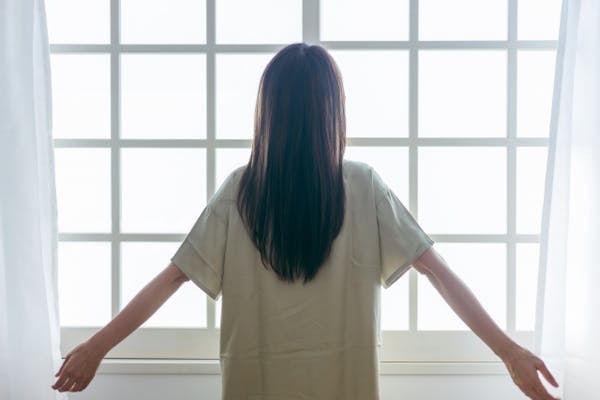 明るい窓際で深呼吸する女性