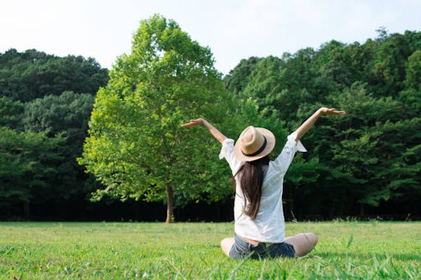 芝生の上に座って空に向かって両手を広げている女性