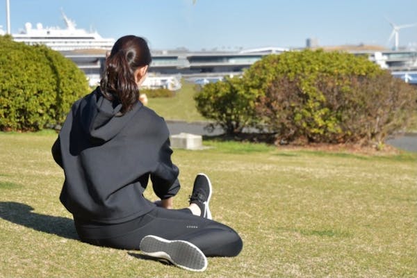 芝生の上でストレッチをする女性の後ろ姿