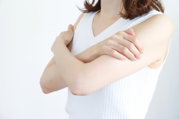 両腕を抱えるタンクトップの女性