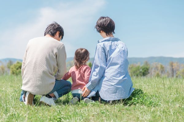 芝生の上でくつろぐ核家族の後ろ姿