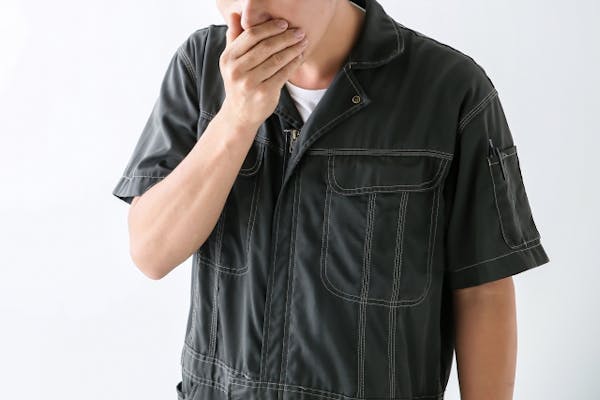 口元を手でおさえる作業着の男性