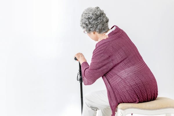 椅子に座ったまま肩をおさえて杖をついた高齢者