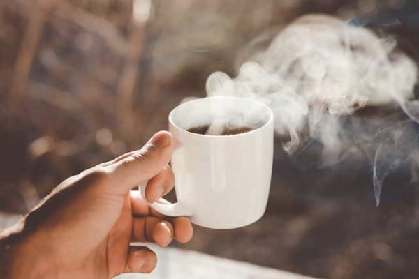 手に持ったホットコーヒーのカップ