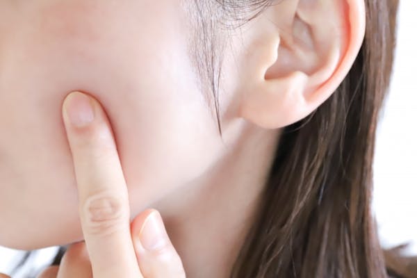 自分の頬を指で押している女性