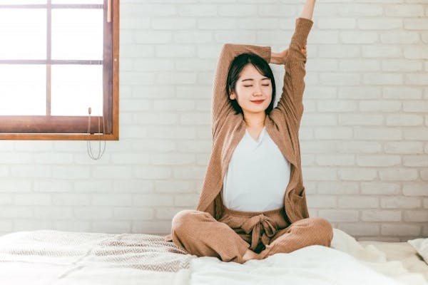 ベッドの上で背伸びをする女性