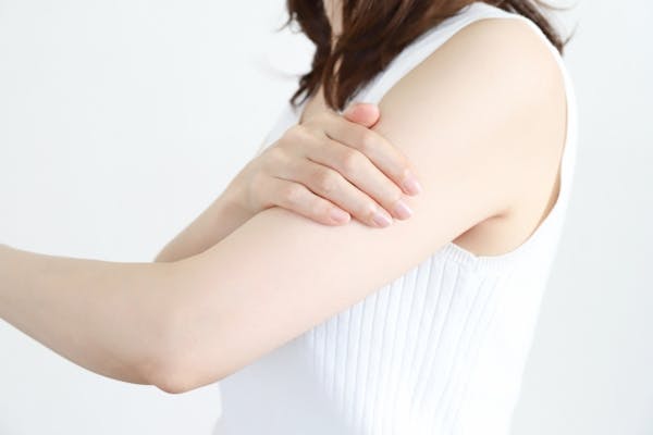 自分の二の腕に手をあてる女性