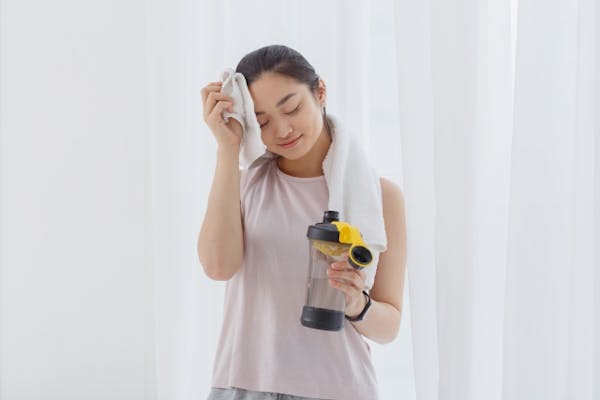 運動後汗を拭きながら水分補給をする女性