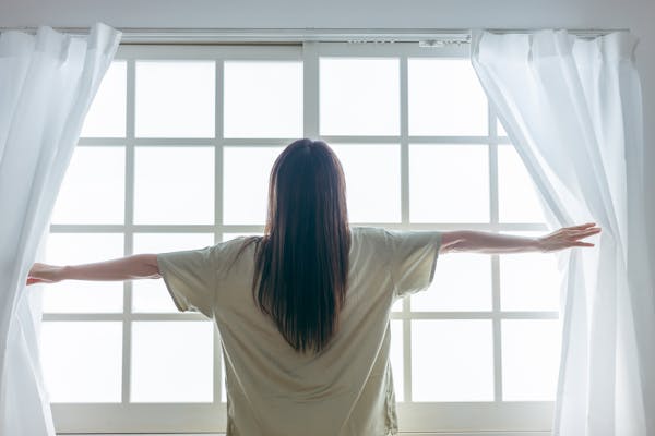 カーテンを開ける女性の後ろ姿