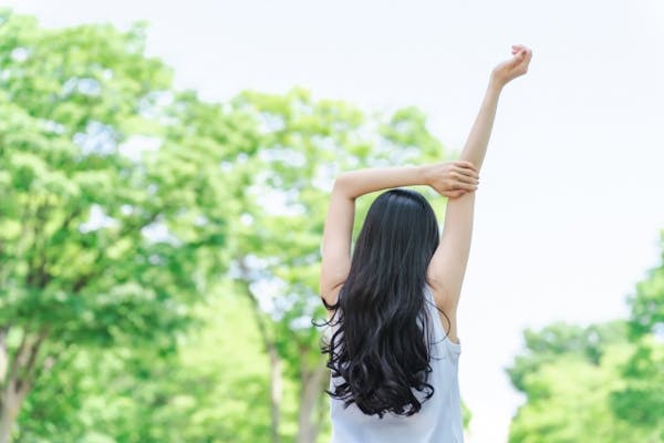 新緑の中背伸びをする女性の後姿