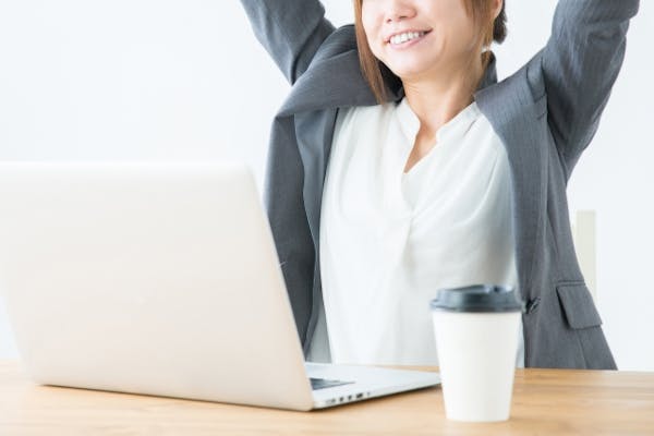 ノートパソコンの前で背伸びする女性