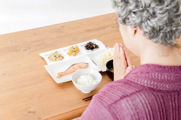 食事の前で手を合わせる高齢女性