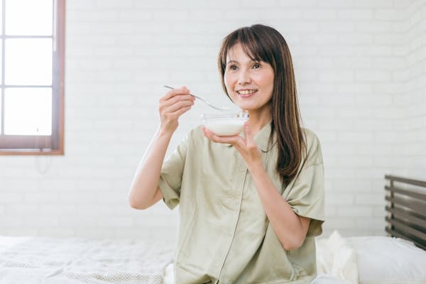ベッドに座ってヨーグルトを食べる女性