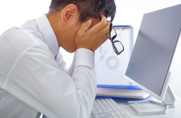 パソコンの前でメガネを取って眠そうな男性