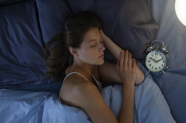 目覚まし時計を横に置いてベッドで寝ている女性