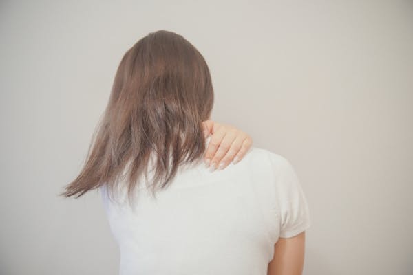 自分の右肩をおさえる女性