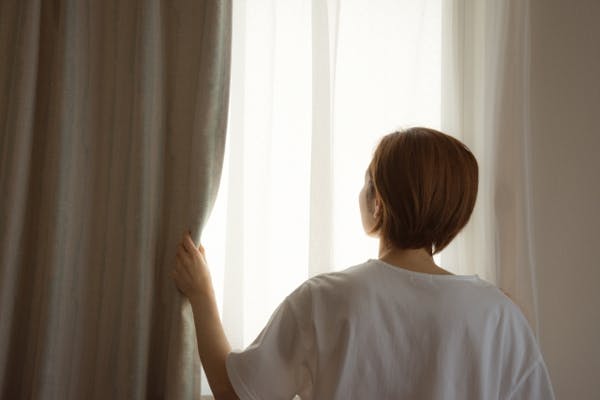カーテンを開ける女性の後ろ姿
