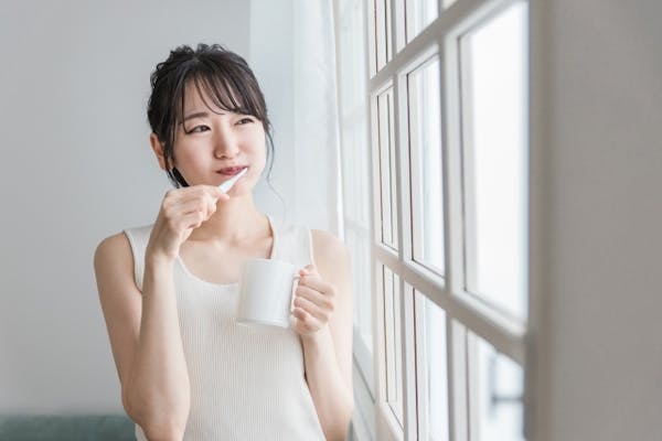 窓辺で歯磨きをする若い女性