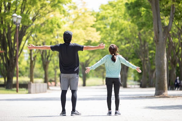 公園で並んで深呼吸している男女の後ろ姿