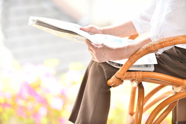 日光を浴びながら椅子に座って新聞を読む高齢者