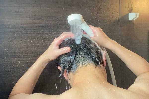 シャワーで髪を洗う男性