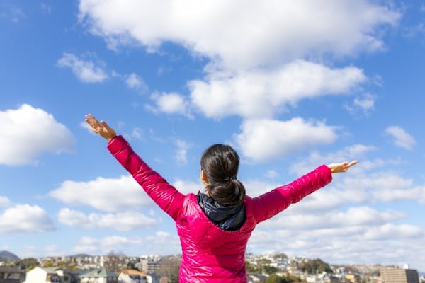 晴天のもとで両腕を広げる女性