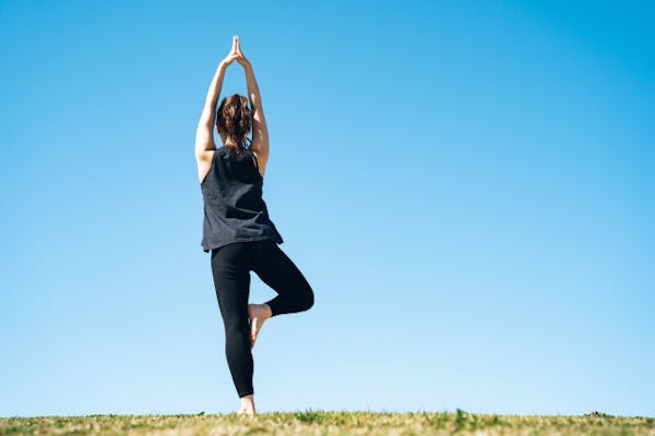 青空の下でヨガをする女性の後ろ姿