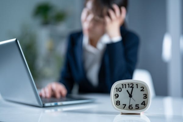 疲れた様子で仕事をするスーツの女性と時計