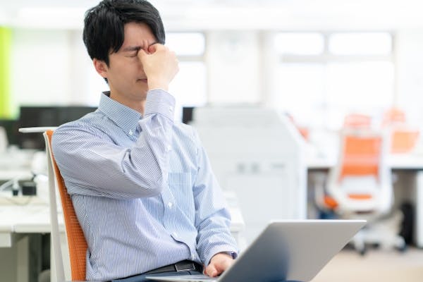 パソコンの前で目頭をおさえる男性